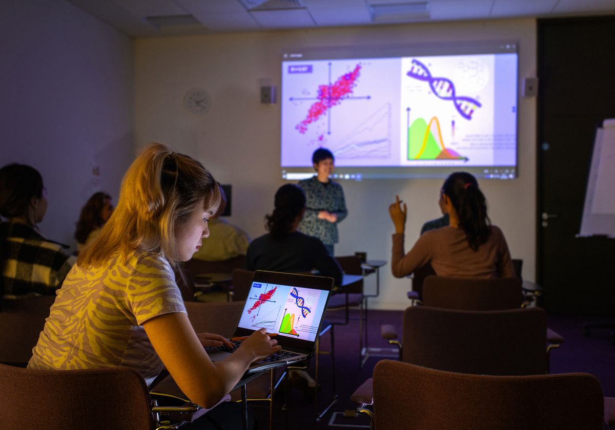 An image of a classroom where a scientist is giving a presentation using a slide deck projected on the wall. An image of a classroom where a scientist is giving a presentation using a slide deck projected on the wall.