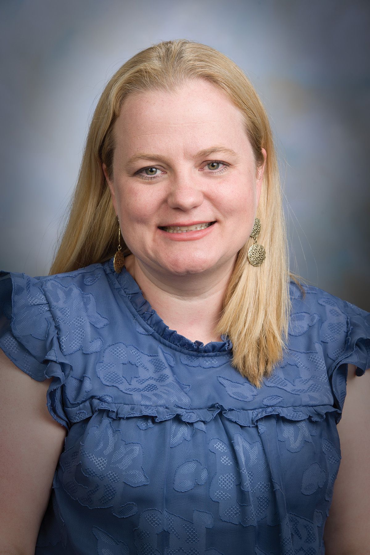 Julie Moreno wears a blue shirt against a grey background. Julie Moreno wears a blue shirt against a grey background.