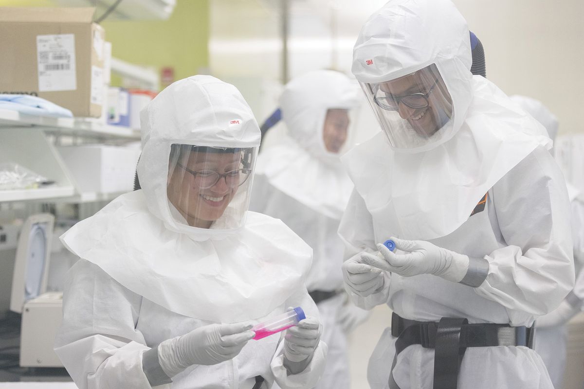 Arinjay Banerjee and a fellow researcher wear white suits with clear face plates and hold test tubes. Arinjay Banerjee and a fellow researcher wear white suits with clear face plates and hold test tubes.