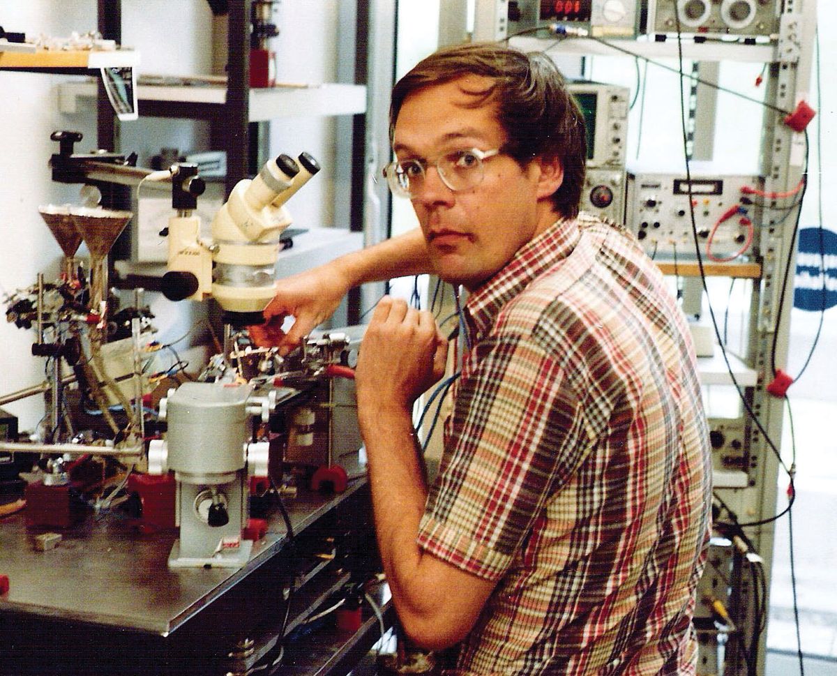 A man stands in front of a microscope setup. A man stands in front of a microscope setup.