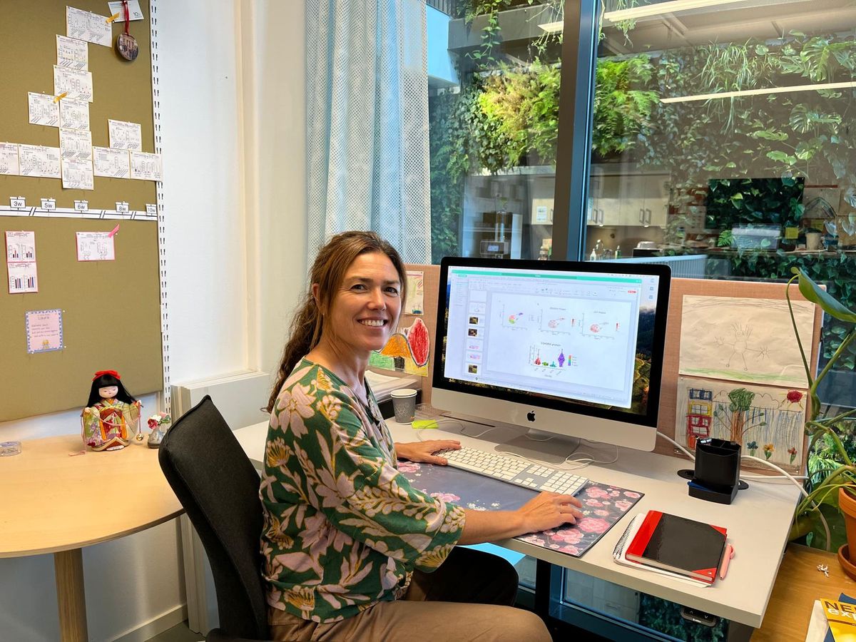Itziar Martinez-Gonzalez, an immunologist at the Karolinska Institute, wears a green and pink floral-printed shirt sitting at her desk. She is turned to smile at the camera. Itziar Martinez-Gonzalez, an immunologist at the Karolinska Institute, wears a green and pink floral-printed shirt sitting at her desk. She is turned to smile at the camera.