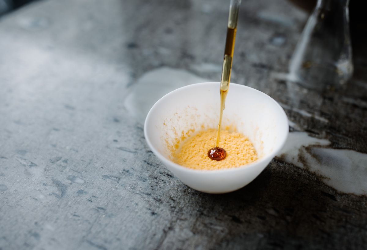 Photo of an orange rice custard in a white bowl with an eye dropper releasing a sweet brown syrup to the dessert. Photo of an orange rice custard in a white bowl with an eye dropper releasing a sweet brown syrup to the dessert.