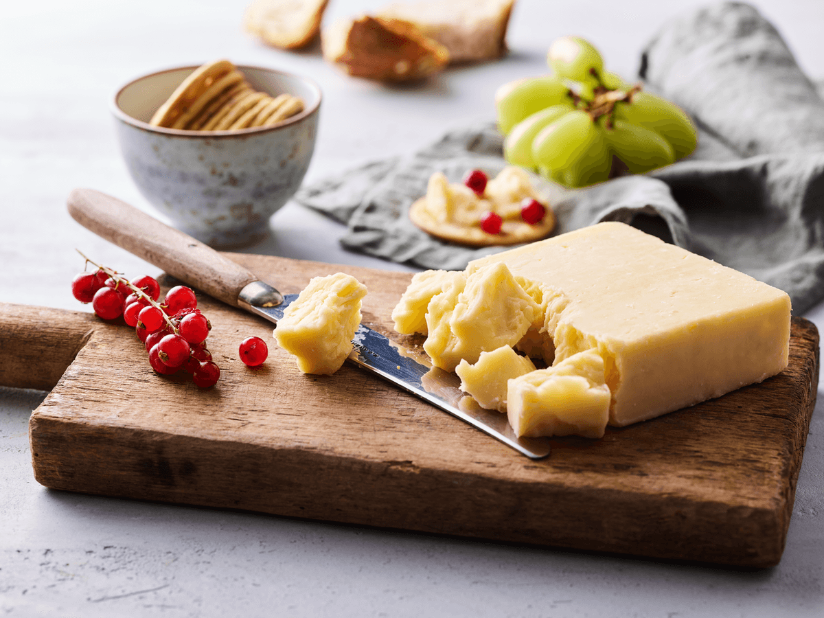 A block of cheddar cheese is pictured with various accompaniments. A block of cheddar cheese is pictured with various accompaniments.